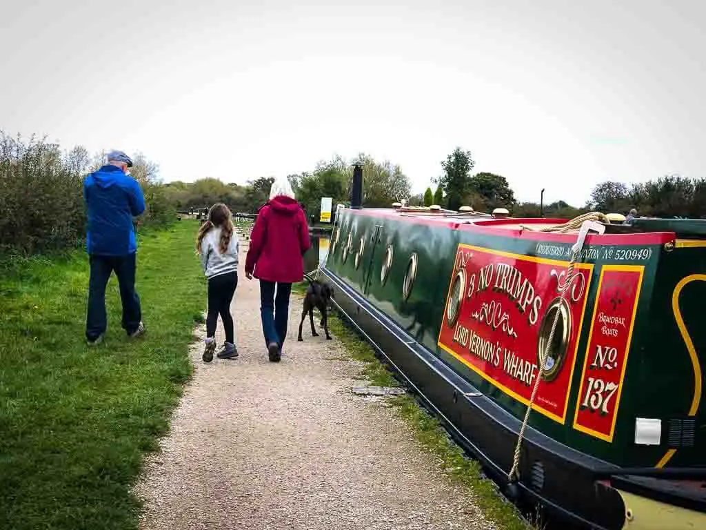 family of three and dog walking past a bright canal boat