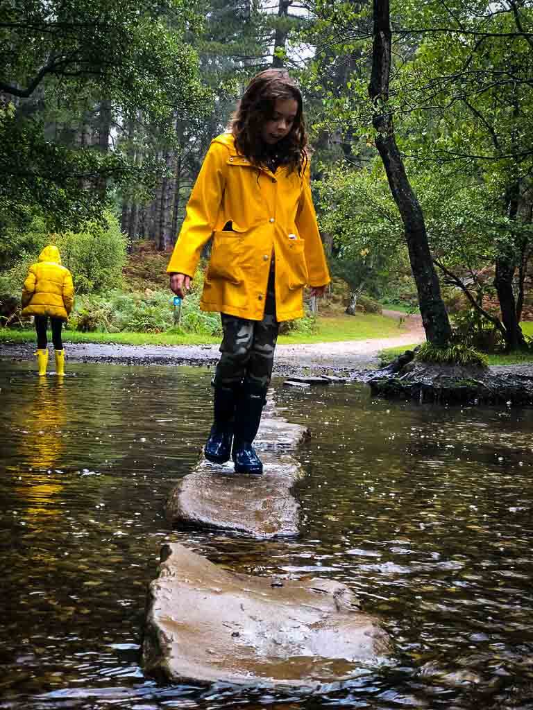 girl in yellow coat standing on stepping stone