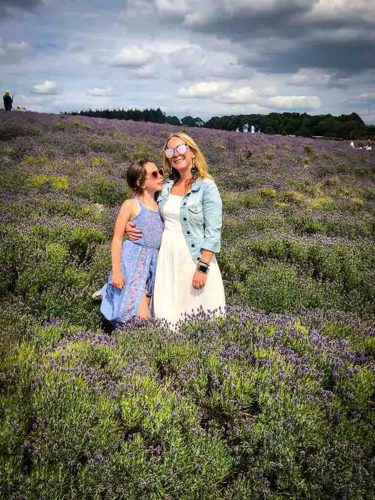 girl in lilac dress with arms around mum in white dress and denim jacket and sunglasses in a lavender field
