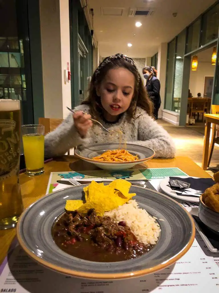 beef chilli, nachos and rice with girl eating pasta in background