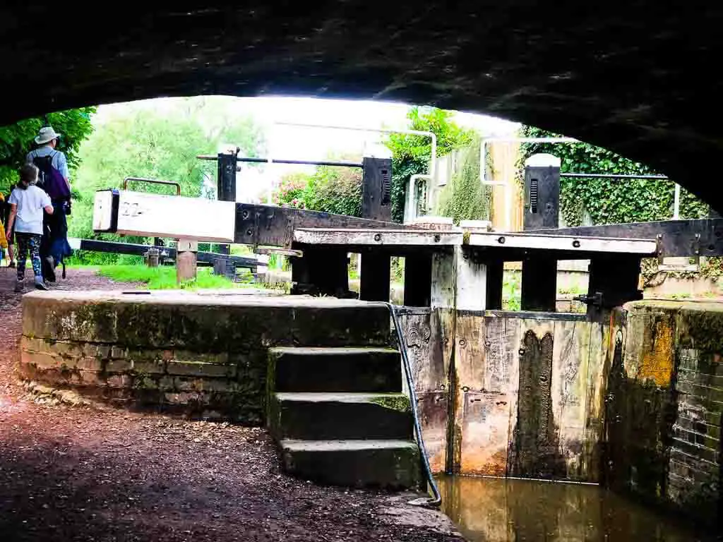 walking under a canal bridge with a black and white lock at the far end