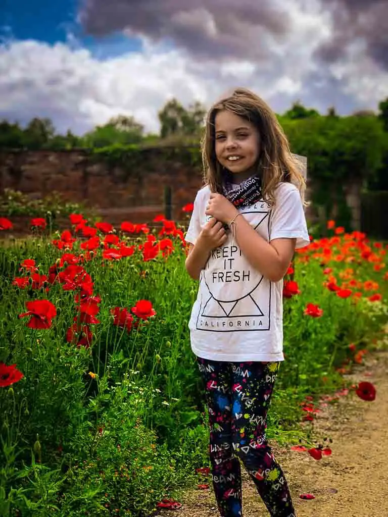 girl standing infront of bright red poppies. she is smiling