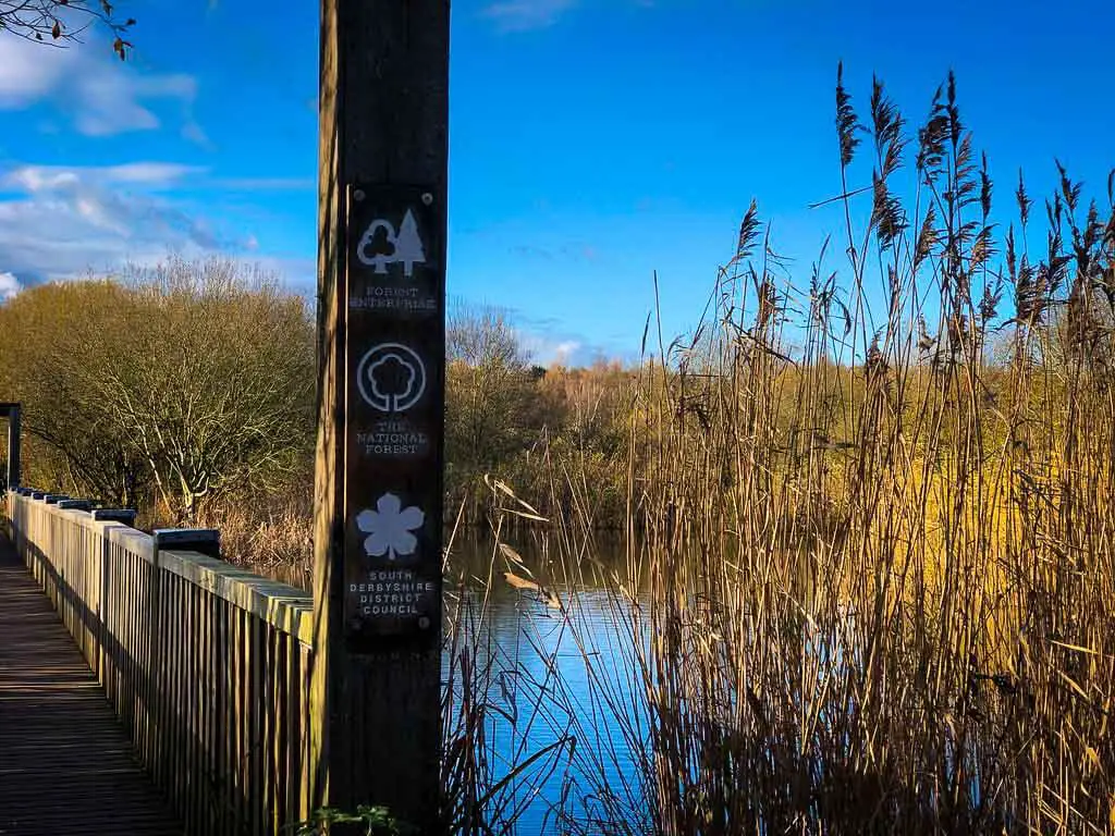 sign at rosliston forestry centre infront of a lake with brown reeds