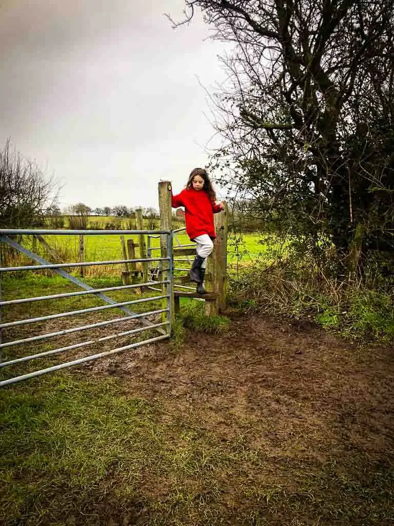 girl crossing over stile next to a metal gate