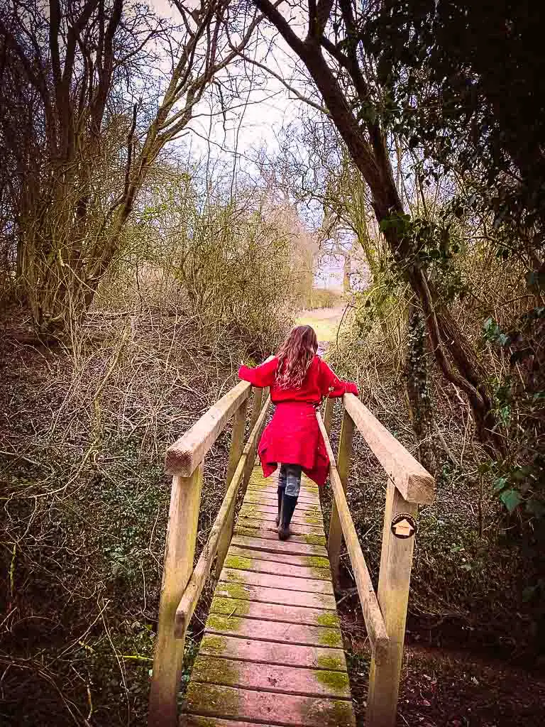 young girl in red jumper and wellies crossing over a wooden bridge
