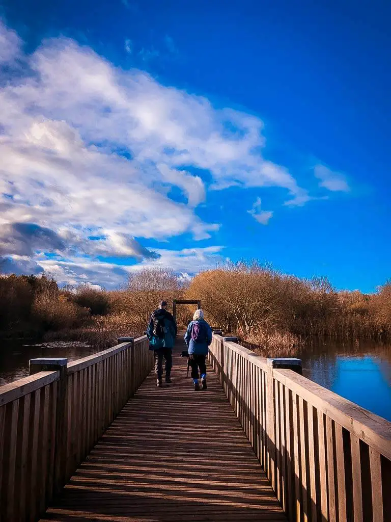 two hikers walking across a wooden bridge under very blue sky