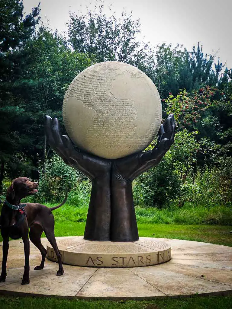 dog standing next to a memorial with a globe in two hands
