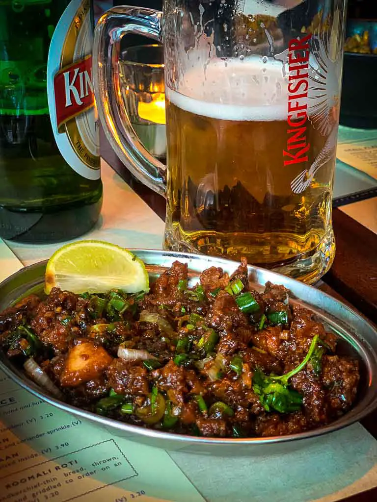 bowl of chilli chicken infront of a large jug of kingfisher beer