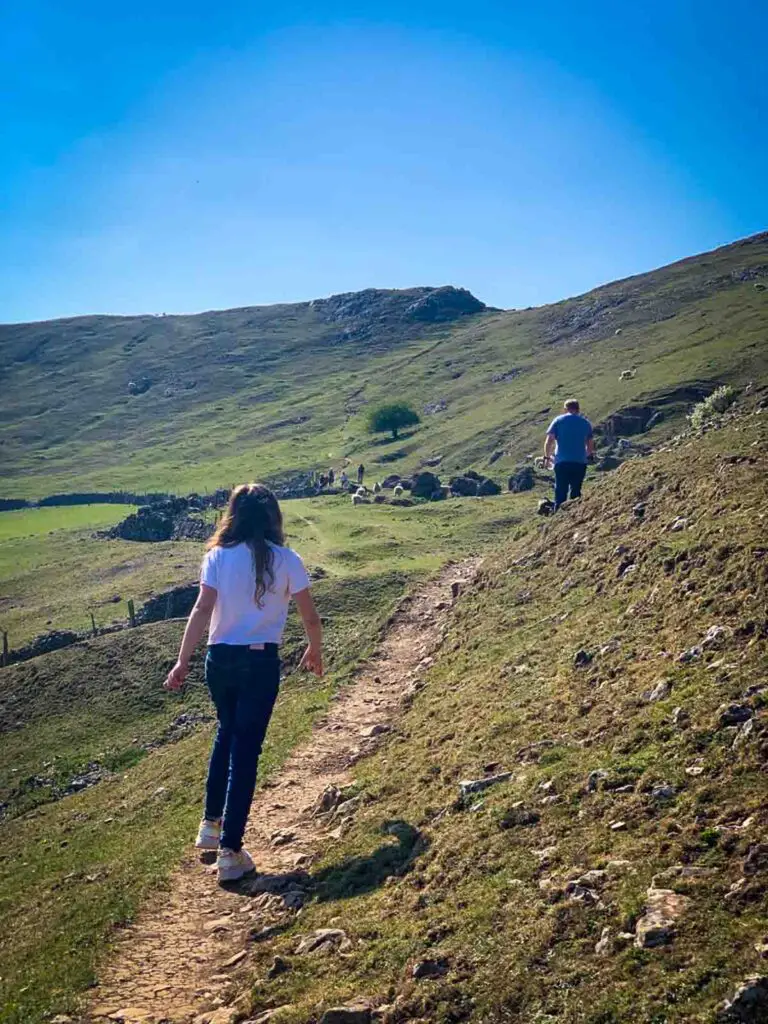 girl in white t-shirt walking across a narrow path through the peak district hills