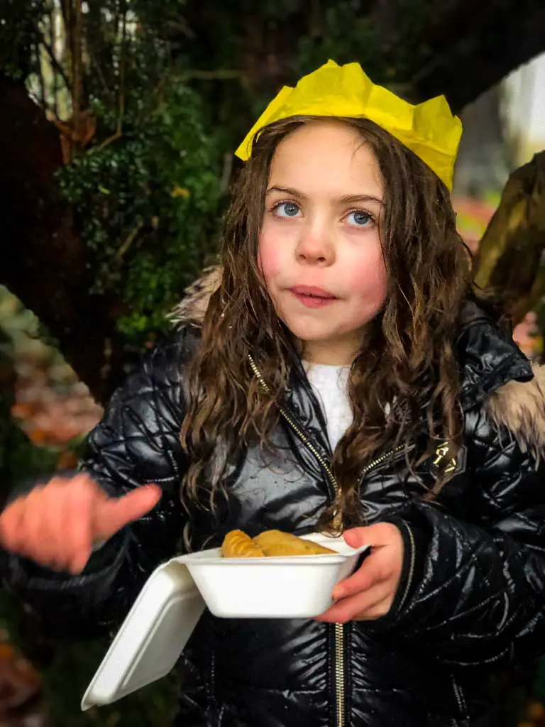 girl in big coat and yellow paper party hat eating a cornish pasty in the rain