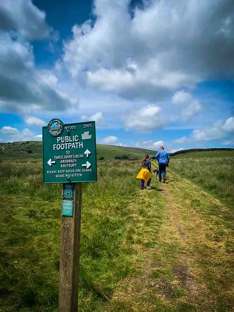 green footpath sign directing walkers along the trail to three shires head