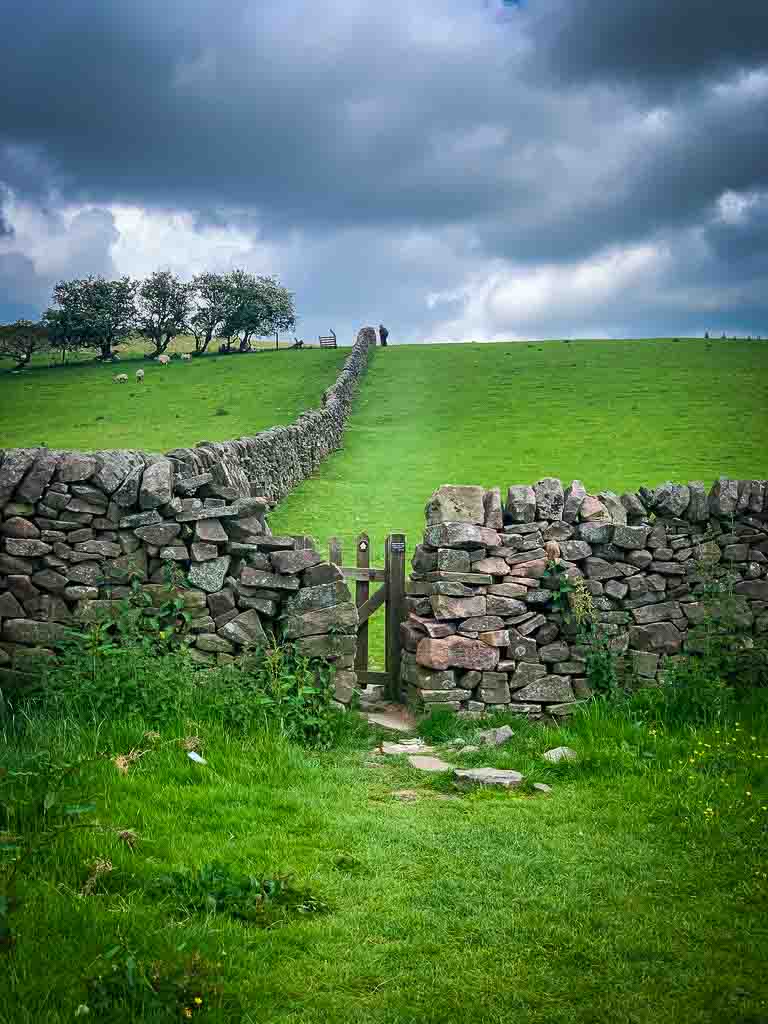 narrow wooden gate between a stone wall at the bottom of a bright green field