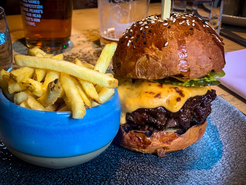 huge cheeseburger with melted cheese and blue bowl of fries