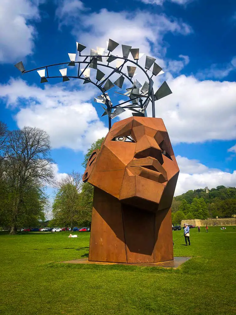 huge rusty head sculpture with silver flying books flying from the top
