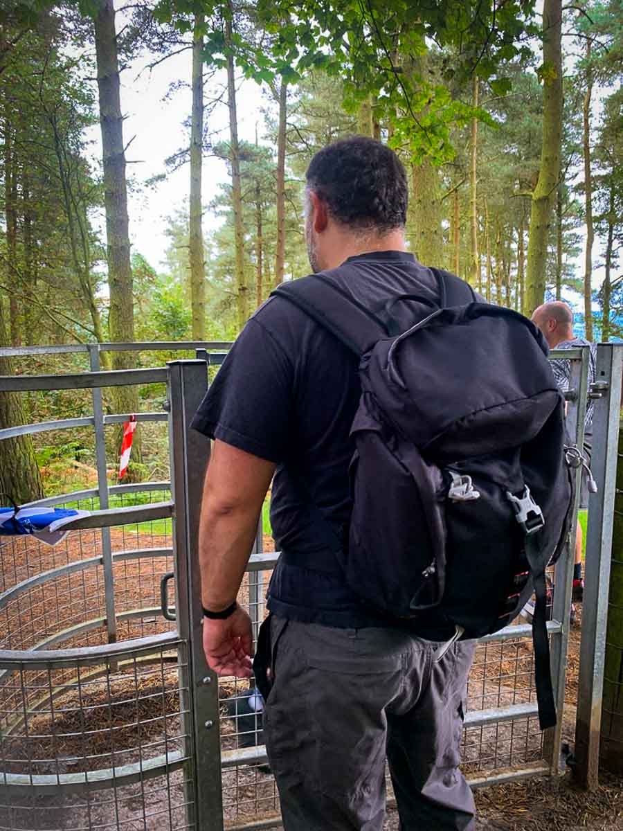 man in black t-shirt and backpack going through a metal kissing gate