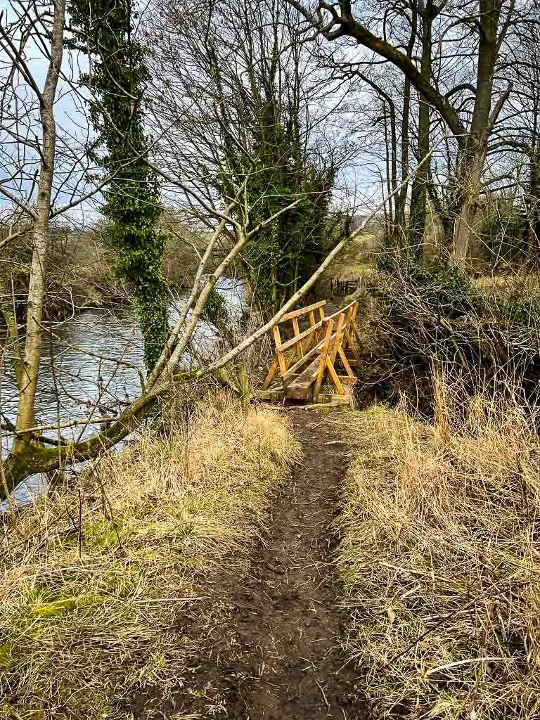 new wooden bridge with muddy path next to the river dove